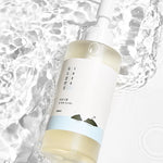 Round Lab 1025 Dokdo Cleansing Oil partially submerged in water, featuring a minimalist design and nature-inspired artwork.