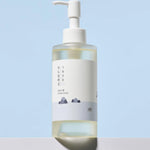 Round Lab 1025 Dokdo Cleansing Oil with a minimalist design, displayed against a pastel blue background, featuring a mountain silhouette on the label.