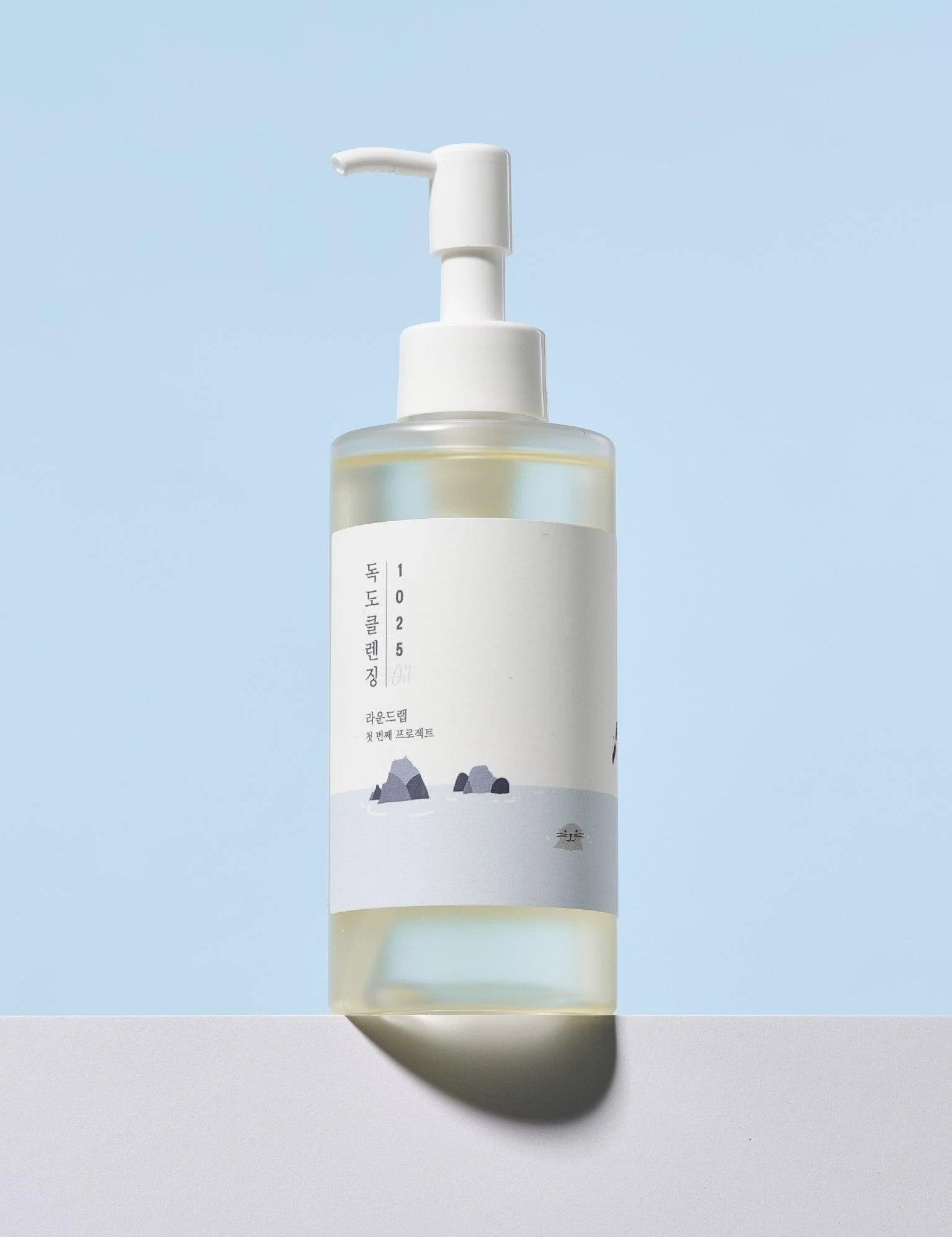 Round Lab 1025 Dokdo Cleansing Oil with a minimalist design, displayed against a pastel blue background, featuring a mountain silhouette on the label.