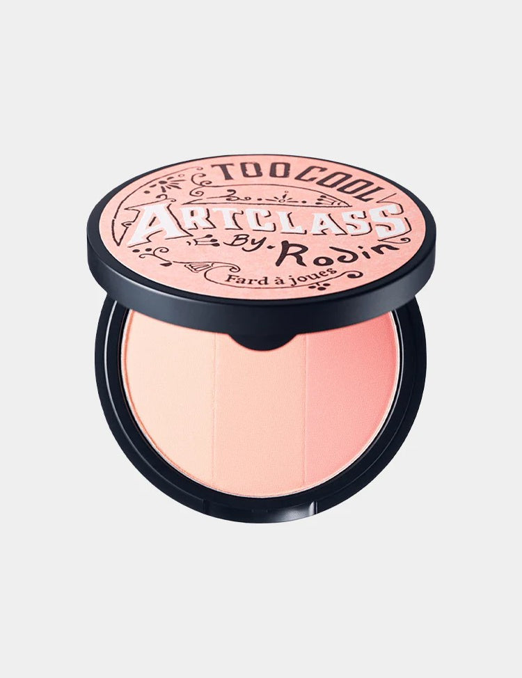 Too Cool for School Artclass By Rodin Blusher in De Peche shade, with its decorative round lid design, perfect for a peach-toned makeup look.

