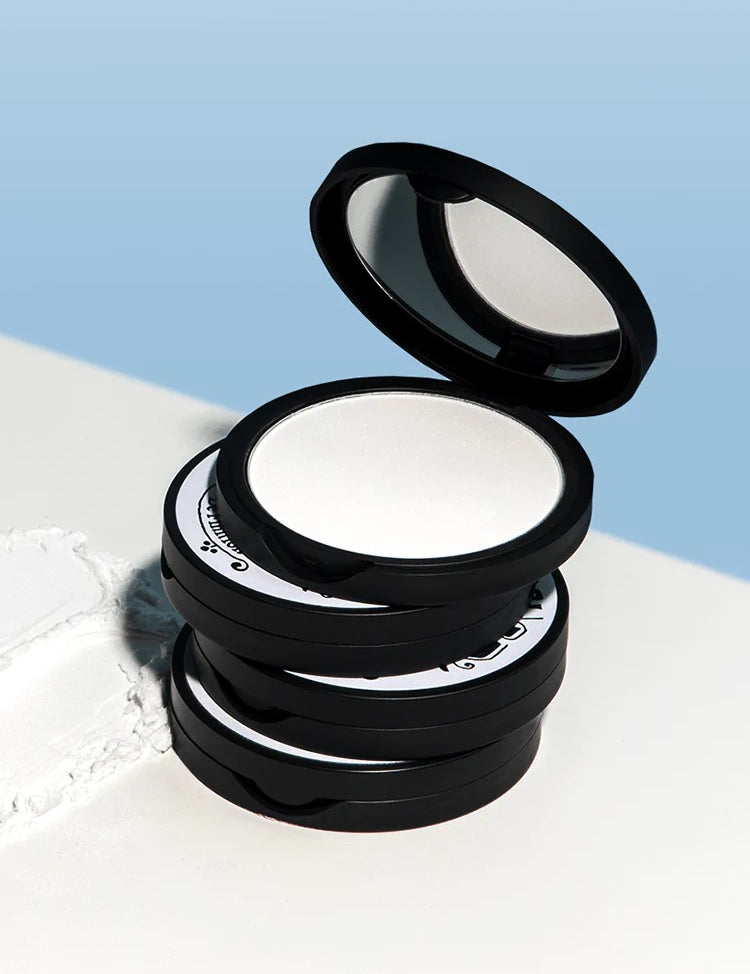 A stack of four Too Cool for School Artclass By Rodin Finish Setting Pact cases, with one case open to reveal the smooth white powder inside, displayed against a soft blue background.