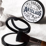 Close-up of Too Cool For School Art Class by Rodin Finish Setting Pact, paired with a makeup brush, resting on a soft white towel for a clean and polished aesthetic.