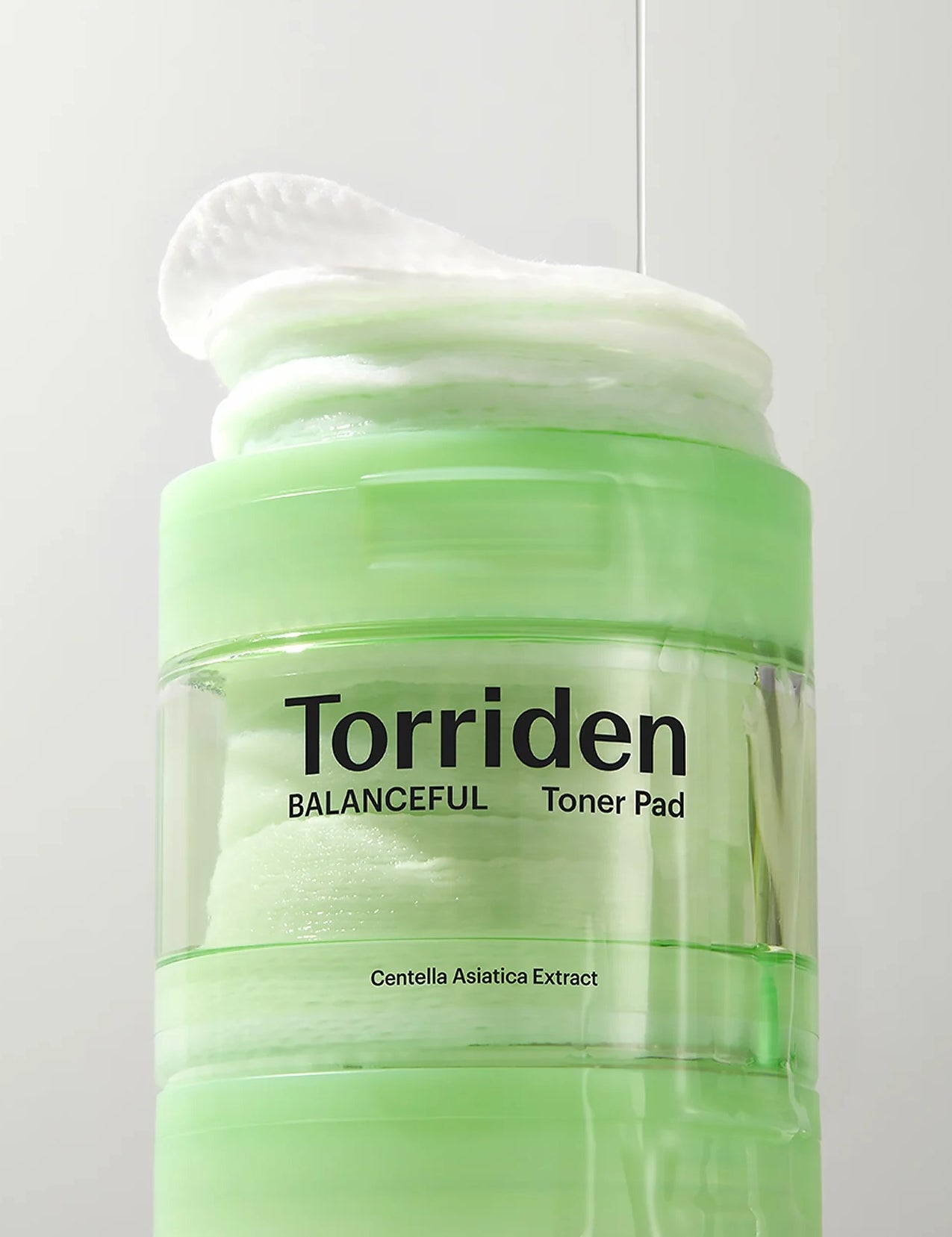 Green jar of Torriden Balanceful Toner Pad next to a stack of its white pads, with the label highlighting Centella Asiatica Extract for soothing and hydration.