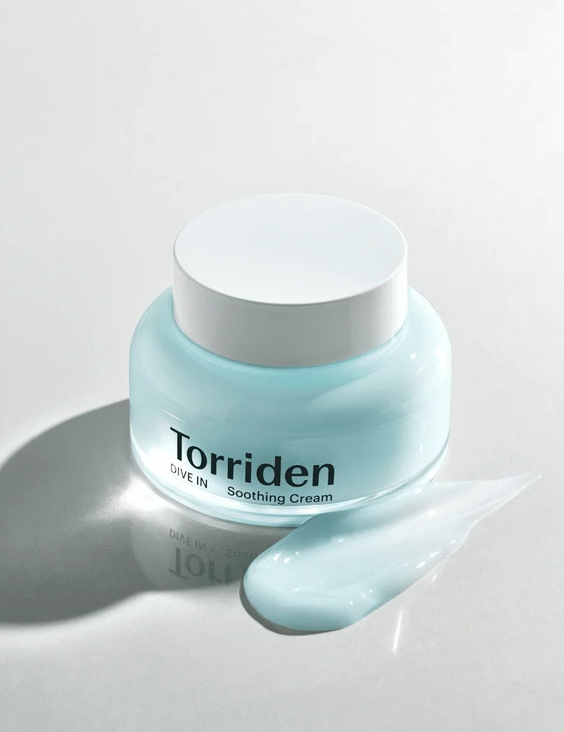 Jar of Torriden Dive In Low Molecular Hyaluronic Acid Soothing Cream in light blue, with a matching cream swatch beside it on a reflective surface.