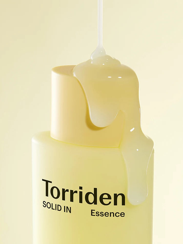 Close-up of a yellow bottle of Torriden Solid IN Essence with glossy essence dripping from the cap against a soft pastel background.